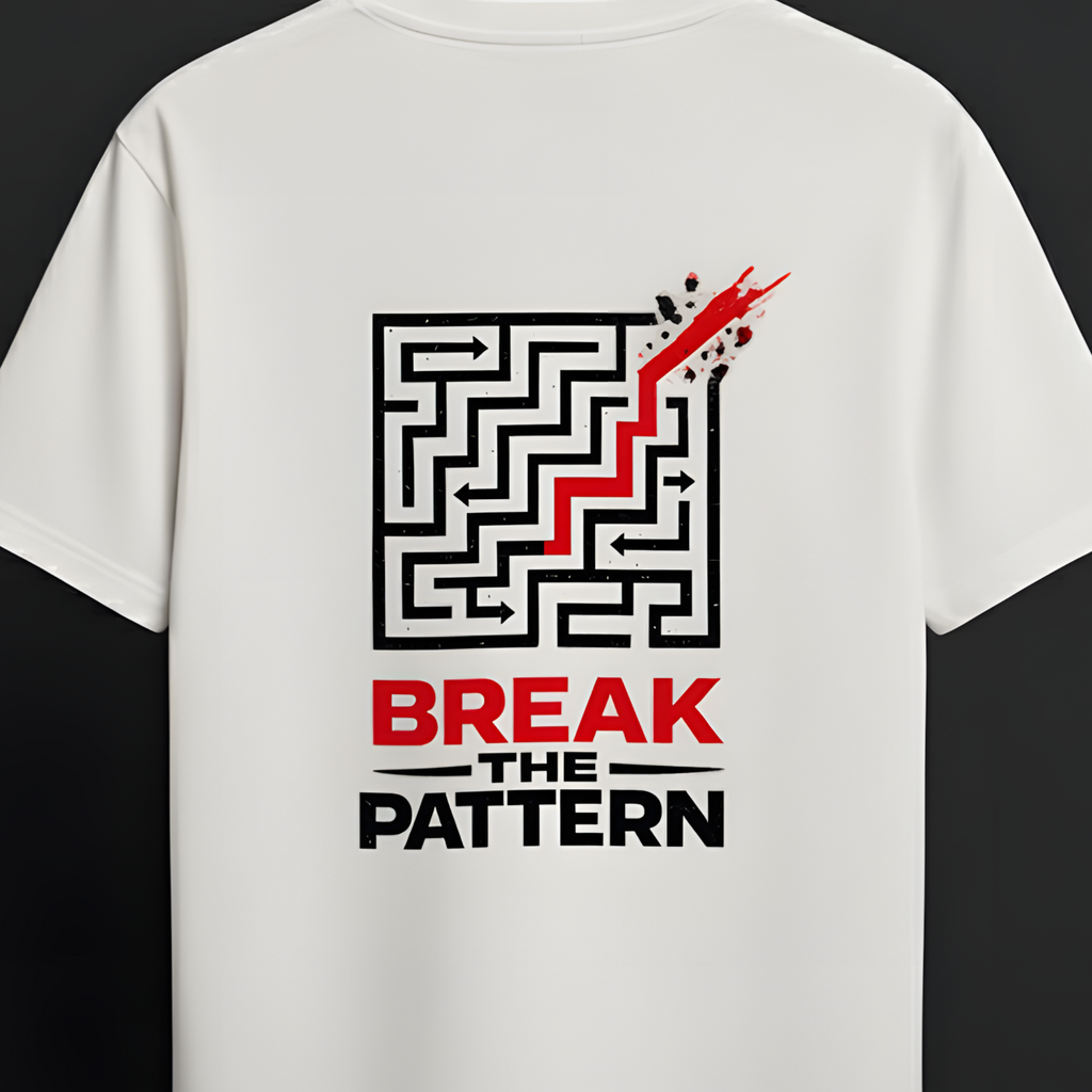 A white short-sleeve t-shirt hanging on a wooden hanger against a dark background. The back of the shirt features a black maze graphic with a red rising line, and the text 'BREAK THE PATTERN' in black and red below.