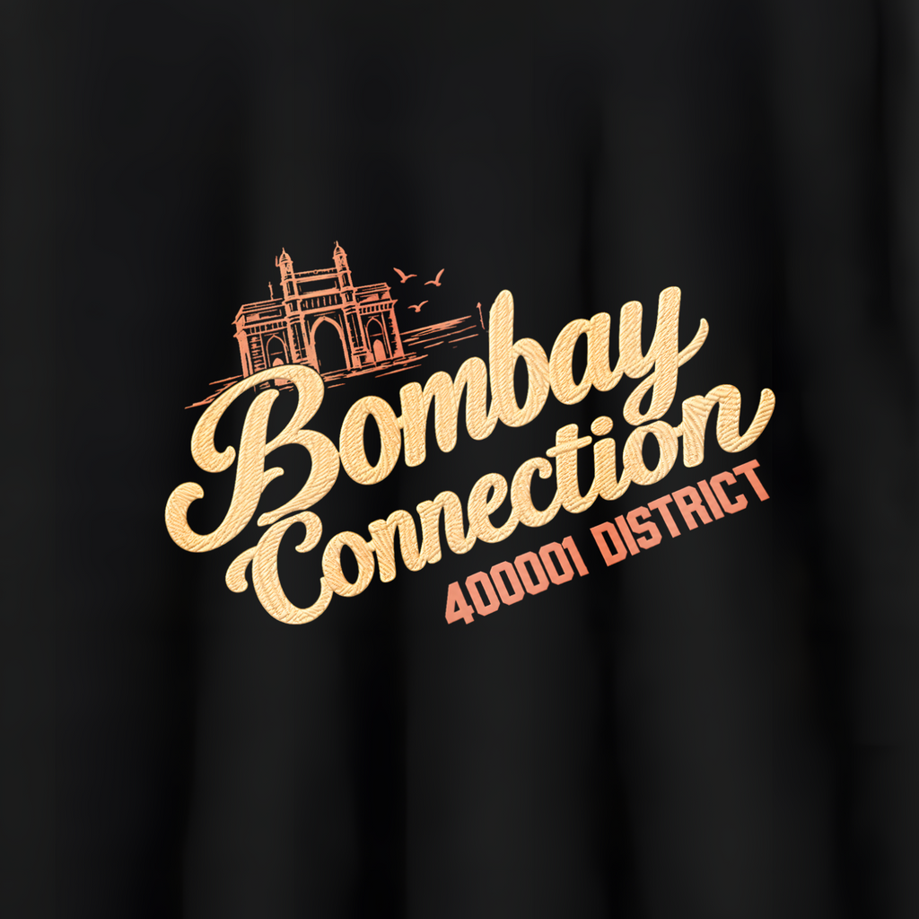 A black short-sleeve crewneck t-shirt hanging on a wooden hanger against a light gray wall. The shirt features a graphic print on the chest with a stylized orange train illustration and the text 'Bombay Connection' in a beige script, with '400012 DISTRICT' printed below in orange.