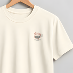 An off-white short-sleeve crewneck t-shirt hanging on a wooden hanger against a neutral gray background. The shirt features a small, delicate pink and orange graphic on the left chest.