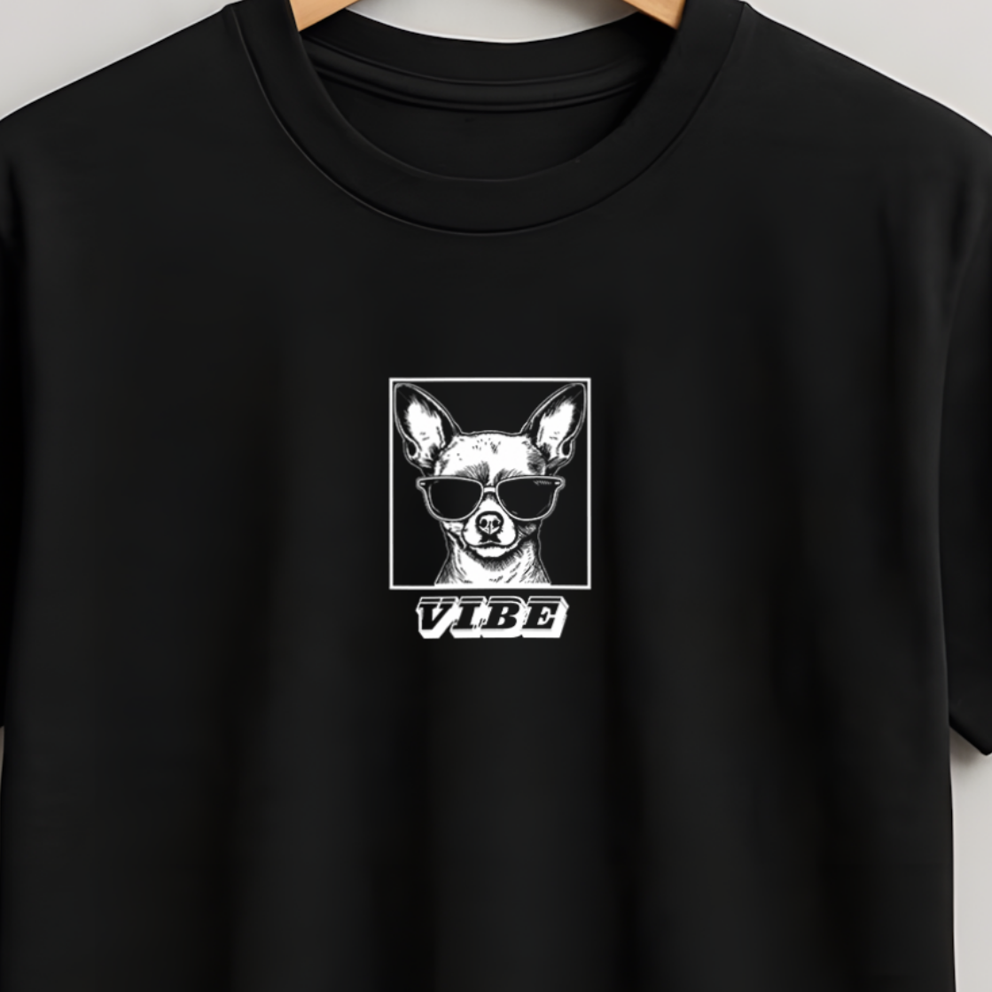 A black short-sleeve crewneck t-shirt hanging on a wooden hanger against a light gray wall. The shirt features a white graphic print on the center chest depicting a dog's face inside a square with the word 'VIBE' underneath.