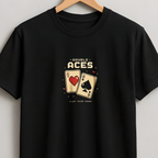 A black short-sleeve crewneck t-shirt hanging on a wooden hanger against a light gray wall. The shirt features a graphic print on the chest depicting two playing cards, an Ace of Hearts and an Ace of Spades, with the text 'A BUNCH OF ACES' above and 'PLAY BACK GAME' below.