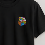 A black short-sleeve crewneck t-shirt hanging on a wooden hanger against a light gray wall. The shirt features a small, colorful graphic of a 3D Rubik's cube printed on the left chest.