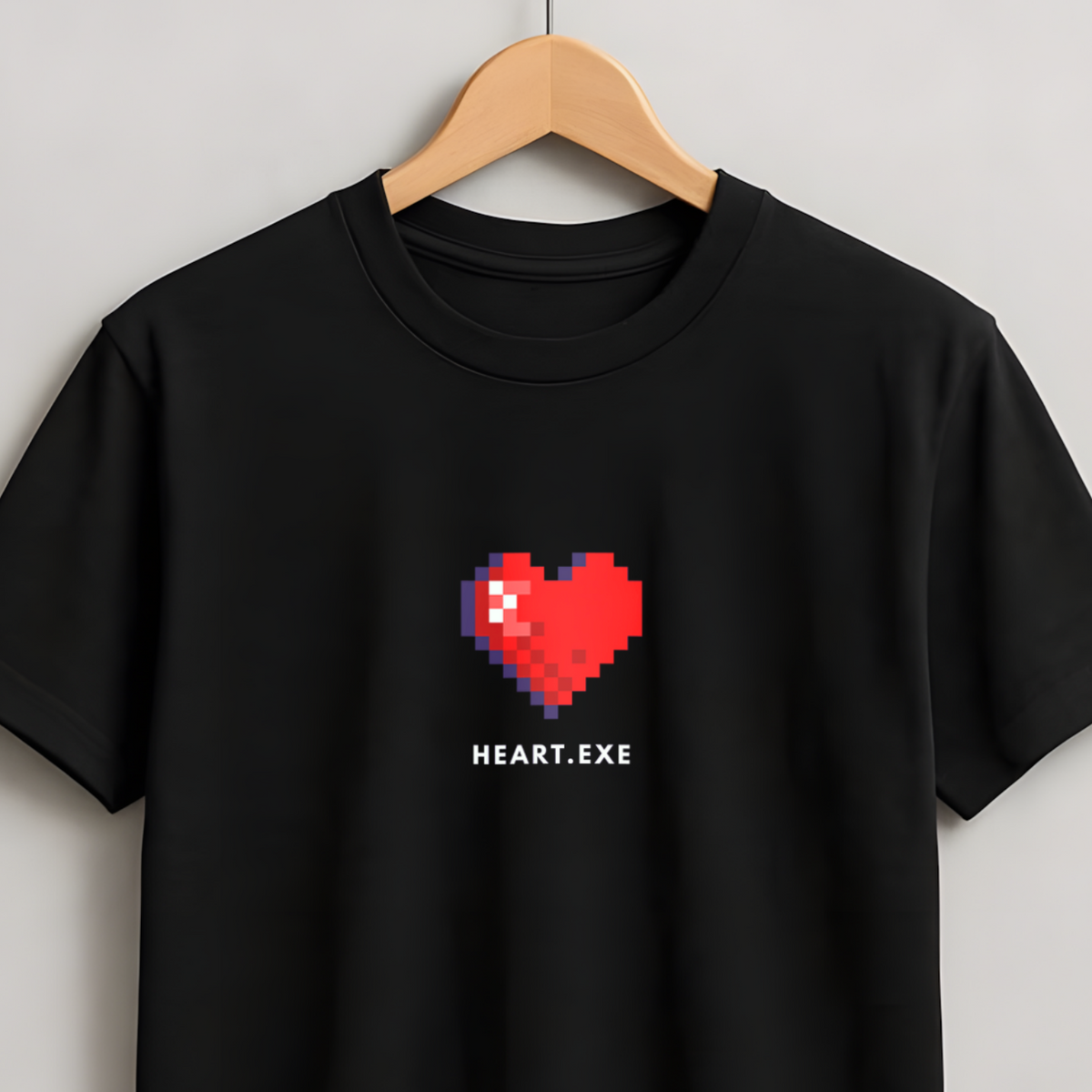 A black short-sleeve crewneck t-shirt hanging on a wooden hanger against a light gray wall. The shirt features a red pixelated heart graphic on the chest with the text 'HEART.