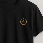 A black short-sleeve crewneck t-shirt hanging on a wooden hanger against a light gray wall. The shirt features a small gold circular logo on the left chest containing a stylized figure.