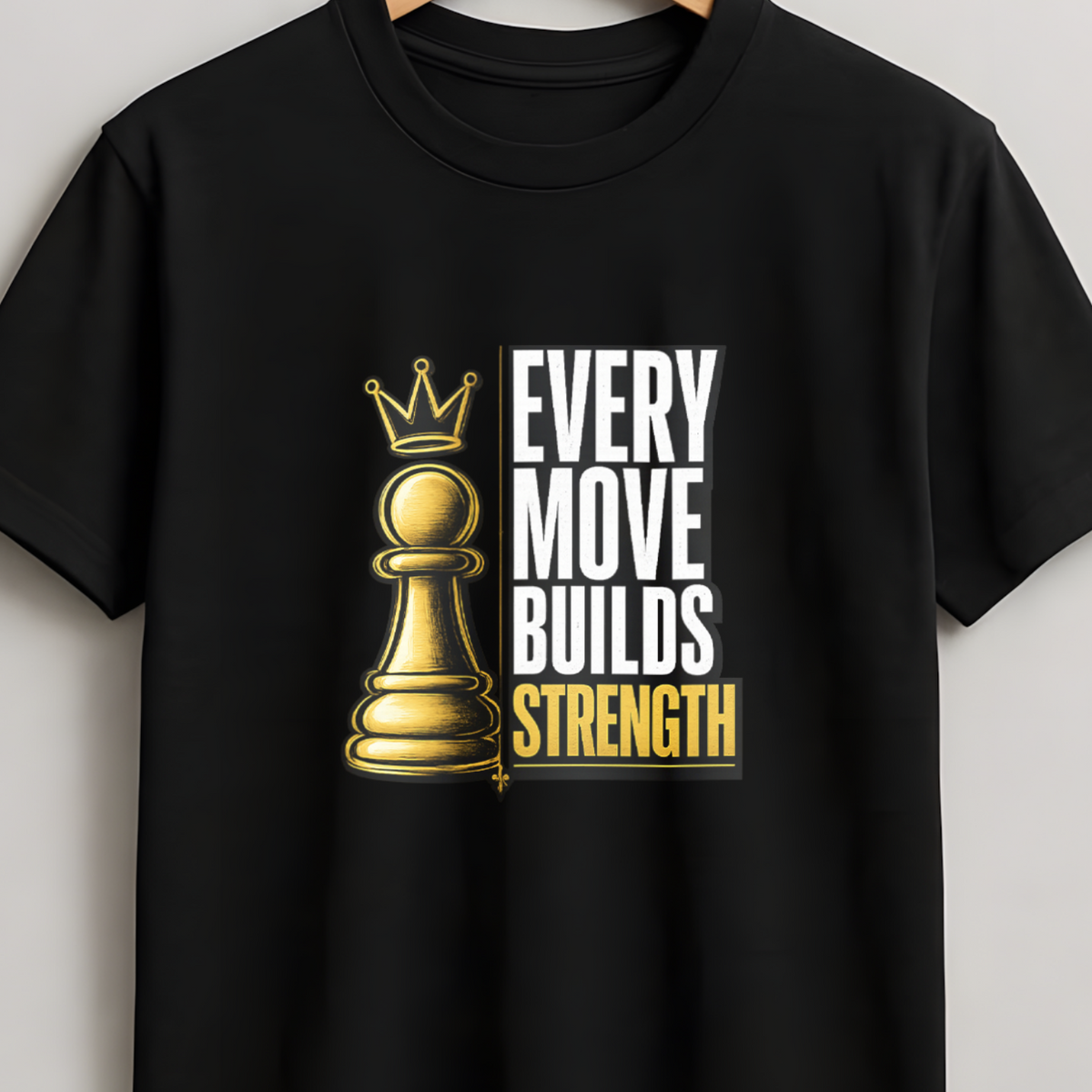 A black short-sleeve crewneck t-shirt hanging on a wooden hanger against a light gray wall. The shirt features a graphic print of a gold chess pawn with a crown next to the text 'EVERY MOVE BUILDS STRENGTH' in white and gold.