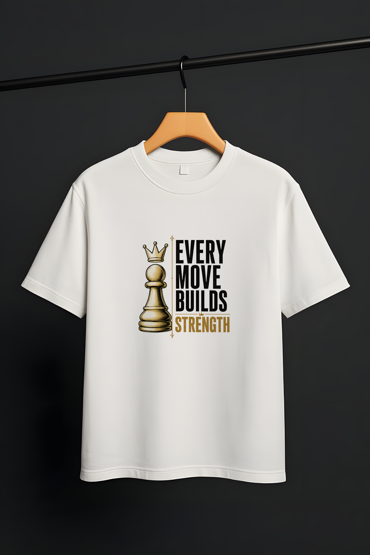 A white short-sleeve crewneck t-shirt hanging on a wooden hanger from a black clothing rack. The shirt features a graphic print of a gold chess queen piece next to the text 'EVERY MOVE BUILDS STRENGTH' in black and gold.