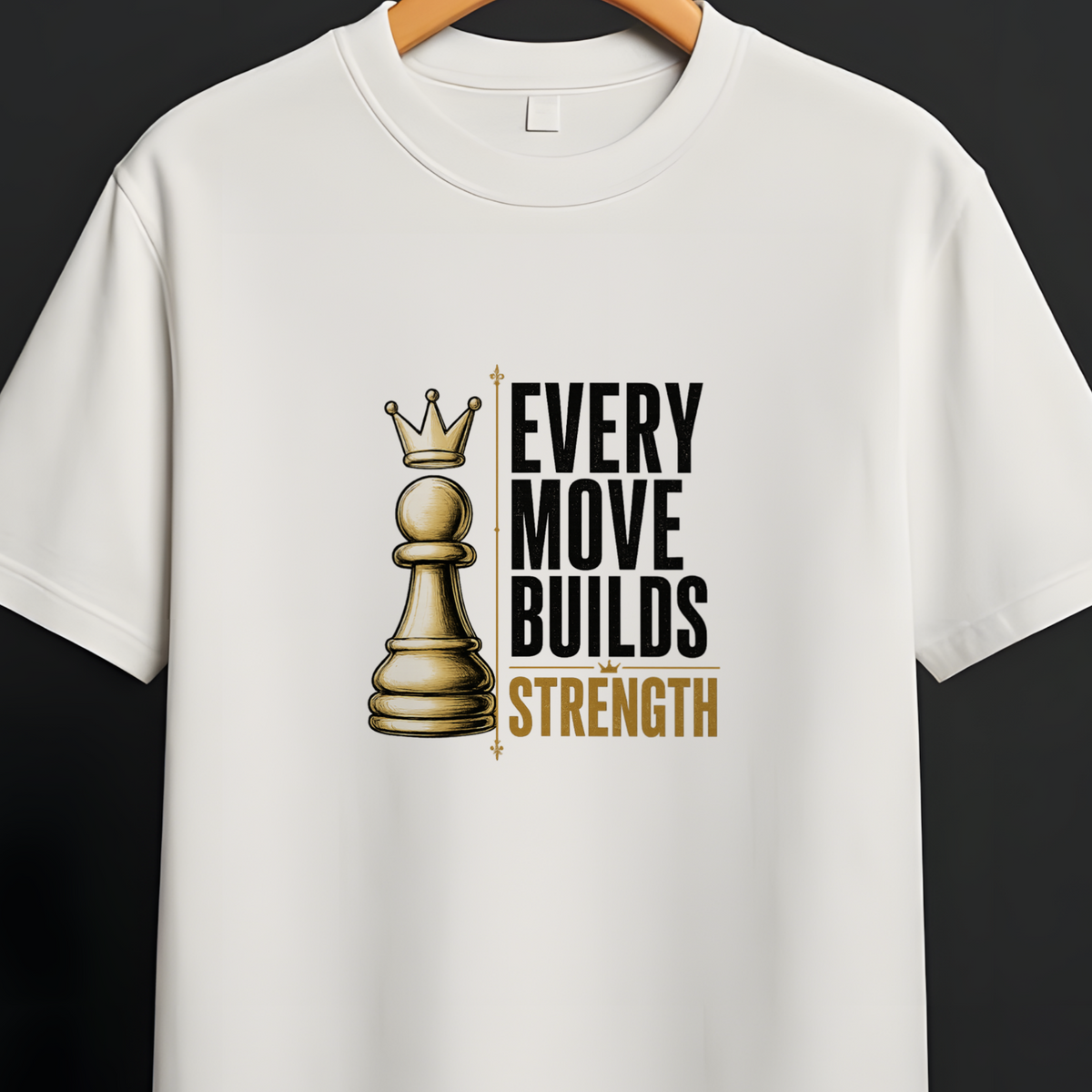 A white short-sleeve crewneck t-shirt hanging on a wooden hanger from a black clothing rack. The shirt features a graphic print of a gold chess queen piece next to the text 'EVERY MOVE BUILDS STRENGTH' in black and gold.