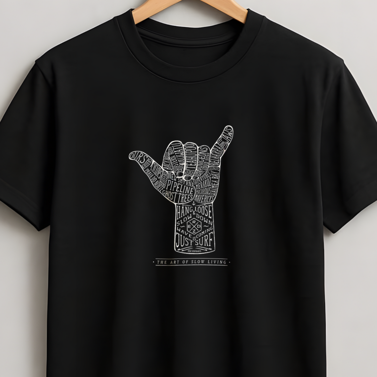 A black short-sleeve crewneck t-shirt hanging on a wooden hanger against a light gray wall. The shirt features a white graphic of a hand sign with intricate patterns inside, and the text 'THE SHIT IS GETTING EASY' printed below it.
