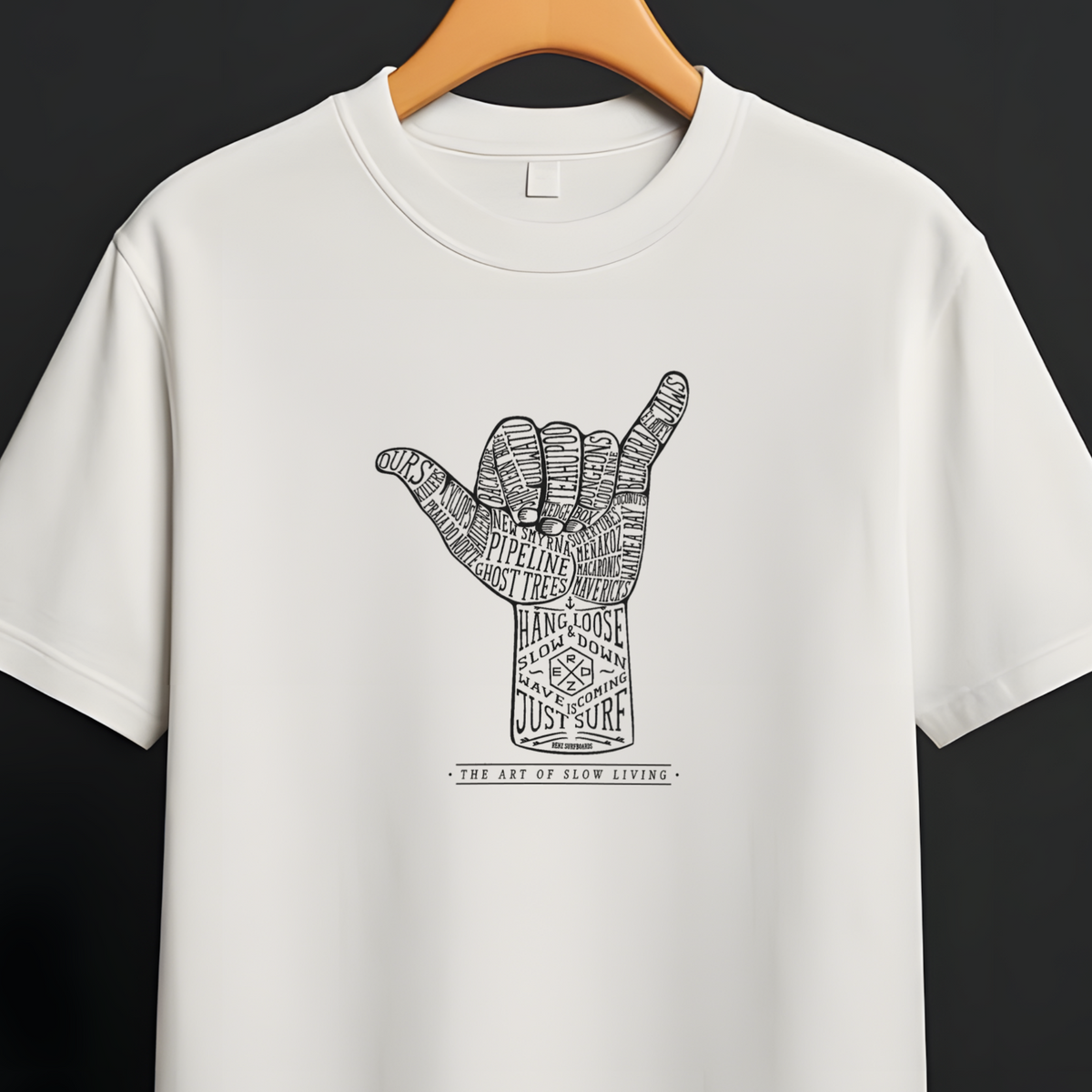 A white short-sleeve crewneck t-shirt hanging on a wooden hanger from a black clothing rack against a dark gray background. The shirt features a black graphic of a hand in a shaka sign pose, filled with intricate patterns, and the text 'THE ART OF LUCK WORE' printed below it.