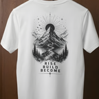 A white short-sleeve t-shirt hanging on a wooden hanger against a dark brown wood-paneled background. The back of the shirt features a large black graphic print of a mountain, sun, trees, and the text 'RISE BUILD BECOME'.