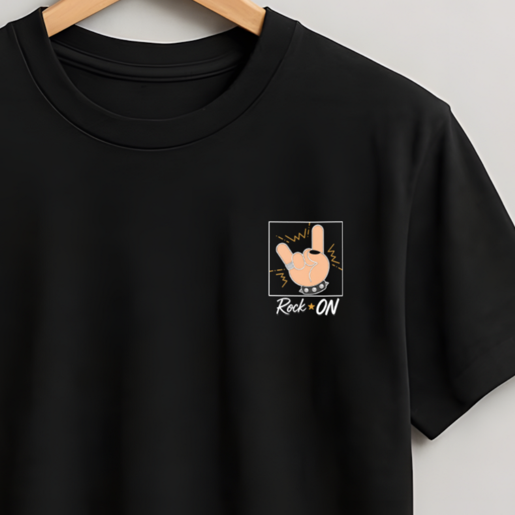 A black short-sleeve crewneck t-shirt hanging on a wooden hanger against a light gray wall. The shirt features a small graphic on the left chest depicting a hand giving a thumbs-up inside a square frame, with the text 'Thumbs Up' and 'ROK-UK' written below.