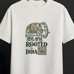 A white short-sleeve crewneck t-shirt hanging on a wooden hanger against a dark gray background. The shirt features a graphic print of an ornate elephant and the text 'ROOTED IN INDIA' in dark green and gold.