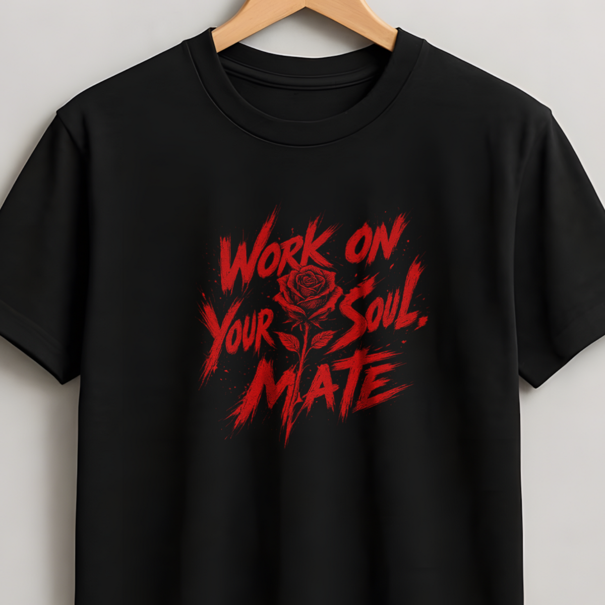 A black short-sleeve crewneck t-shirt hanging on a wooden hanger against a light gray wall. The shirt features a distressed red graphic on the chest with the text 'WORK ON YOUR SOUL.